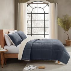 a bed with blue comforter and pillows in front of a window