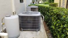 an air conditioner and heat pump on the side of a building next to bushes