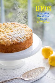 a lemon crumble breakfast cake on a white plate with two lemons next to it