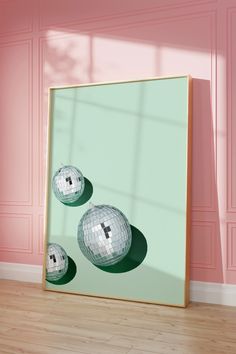 a mirror with three disco balls on it in front of a pink wall and wooden floor