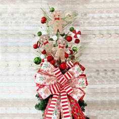 a christmas tree with red and white bows on it's top, decorated with ornaments