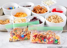 several bags filled with cereal and pretzels sitting on a tray next to bowls of candy