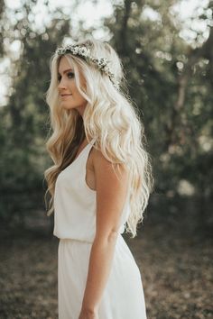 a woman with long blonde hair wearing a white dress standing in the middle of a forest