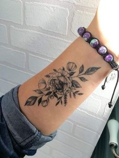 a woman's arm with a flower tattoo on the wrist and beads attached to it