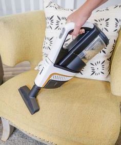 a person is using a vacuum cleaner on a yellow chair with a black and white pillow