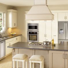 a large kitchen with white cabinets and stainless steel appliances, along with two bar stools