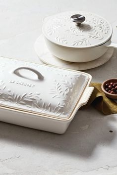 a white casserole dish sitting on top of a table next to a brown bowl