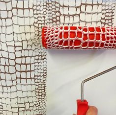 a person using a roller to paint a wall with red and white designs on it