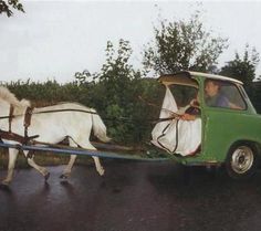 two horses pulling a green car down the road