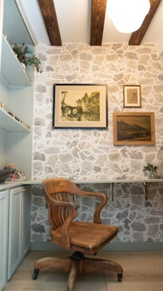 an office chair sitting in front of a stone wall with pictures on the wall above it