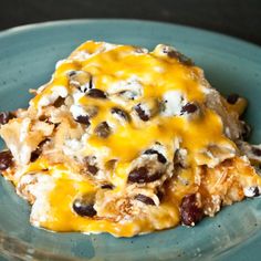 a blue plate topped with an enchilada covered in cheese and black olives