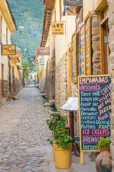 a narrow street lined with stone buildings and signs on the side of each building, along with potted plants