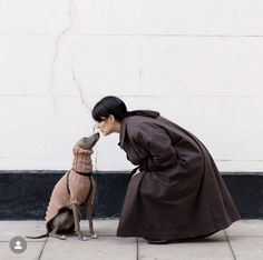 a woman kneeling down next to a dog wearing a sweater