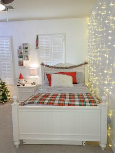 a white bed topped with pillows and blankets next to a window covered in christmas lights