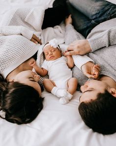 three people laying on top of a bed with a baby in the middle and two adults holding their babies