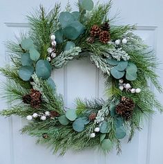 a wreath with pine cones and greenery is hanging on the front door's white door