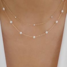 the back of a woman's body wearing a gold chain necklace with white pearls