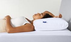 a woman laying on top of a white bed next to pillows and pillowcases