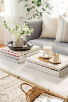 a coffee table topped with books and vases on top of each other next to a couch