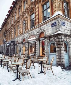 tables and chairs covered with snow in front of an old building on a snowy day