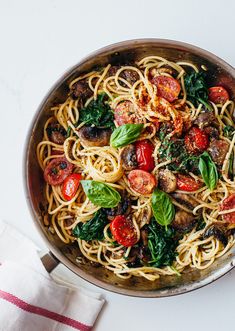 a pan filled with pasta and vegetables on top of a white tablecloth next to a napkin