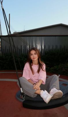 a young woman sitting on top of a swing in a playground next to a building