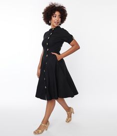 An eye-catching swing dress in solid black. Crafted in a stretchy bengaline and outfitted with an asymmetrical button up front, short sleeves, and side pockets.Available in sizes XS-5X while supplies last. 1950s Black Dress, Uv Clothing, 1950s Outfits, Vintage Inspired Fashion, Weekend Wardrobe, Black Button, Pocket Dress, Unique Dresses, Plus Size Dress