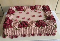 a square cake with pink frosting and red roses on it, sitting on a table