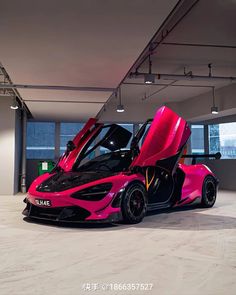 a pink and black sports car parked in an empty garage with its doors open to reveal the interior