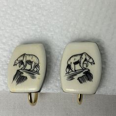 two white and black ceramic wall hooks with bear images on them, one is gold