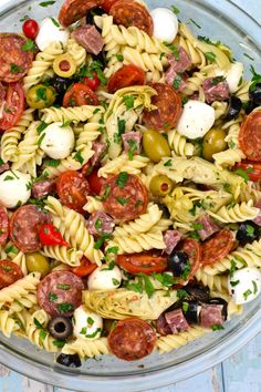 pasta salad with olives, tomatoes, mozzarella and sausage in a glass bowl