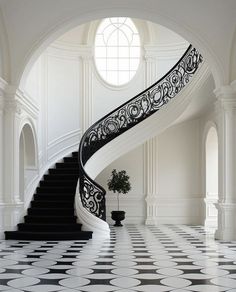 a black and white spiral staircase in an elegant house with tiled flooring, arched windows, and potted plant on the far side