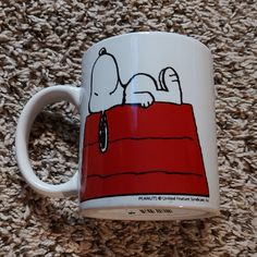 a coffee mug with a snoopy dog on it sitting on a carpeted floor