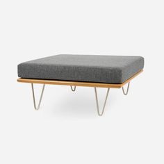 a grey ottoman sitting on top of a wooden frame with two legs and a gray cushion