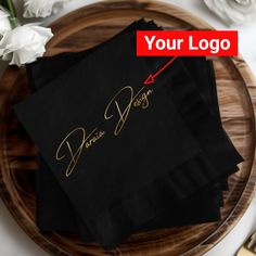 two black napkins with gold foil lettering on them sitting on a wooden platter