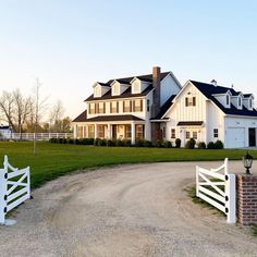 a large white house sitting on top of a lush green field next to a dirt road