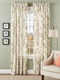 a living room with green walls and floral curtains on the window sill, along with a beige chair