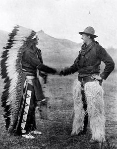 two native american men shaking hands with each other in an open field near mountains and hills