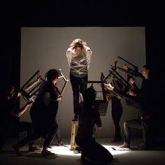 a group of people standing around each other in front of a white wall and black background