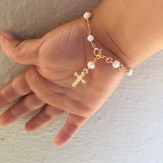 a woman's hand with a cross and pearls bracelet on it, while she is holding the other hand