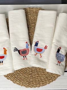 four hand towels with embroidered roosters on them sitting on a wicker place mat