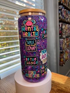 a purple jar with words on it sitting on top of a white stand in front of a window