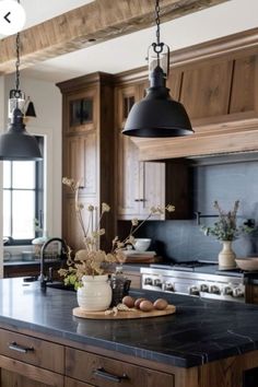 a kitchen with an island and two hanging lights above the stove top, along with wooden cabinets