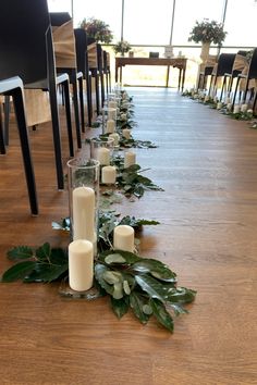 a long table with candles and greenery on the floor in front of it, along with chairs