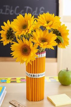 a vase filled with yellow sunflowers sitting on top of a table next to an apple