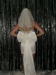 a woman wearing a white dress and veil standing in front of tinsel foil curtain