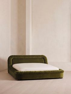 a green couch sitting on top of a wooden floor next to a white wall and window