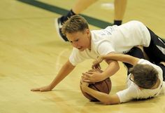 two young boys playing basketball on a court with one falling to the ground while another tries to block him