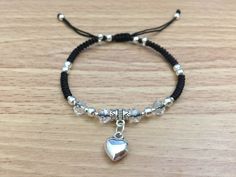 a bracelet with a silver heart charm and black cord on top of a wooden table