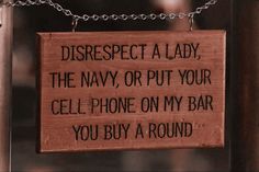 a wooden sign hanging from a chain on a pole that says, disrespect a lady, the navy or put your cell phone on my bar you buy a round